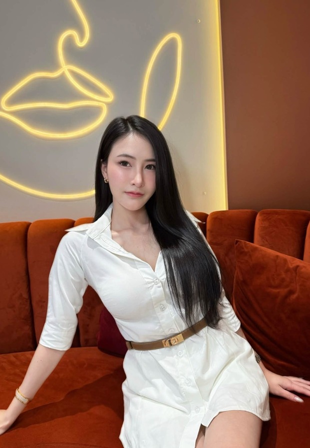 เชิ้ตเดรสสีขาวคาดเข็มขัดน้ำตาลบนโซฟาสีส้มอิฐใต้ไฟนีออน